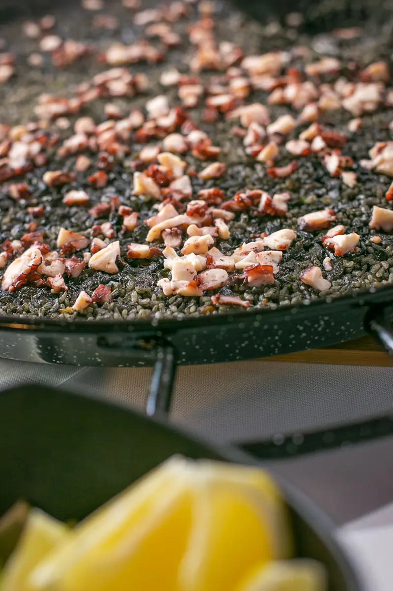Paellera de arroz negro con pulpo en una estación de show cooking